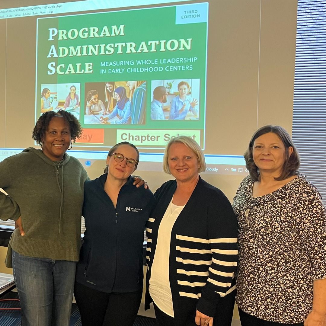 Four people posing in front of a projected “Program Administration Scale” presentation slide