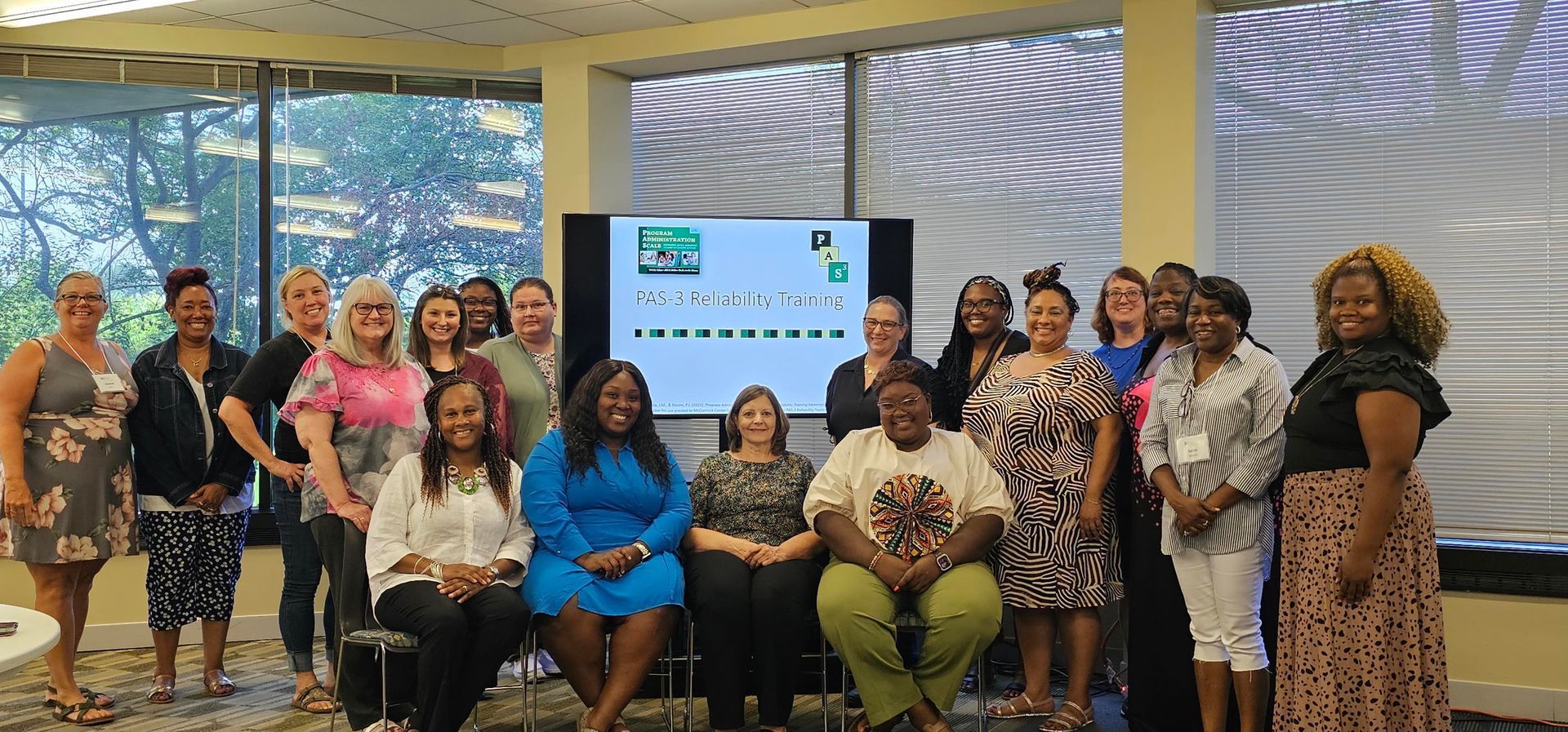 Group of diverse women posing in an office setting with a screen displaying text.