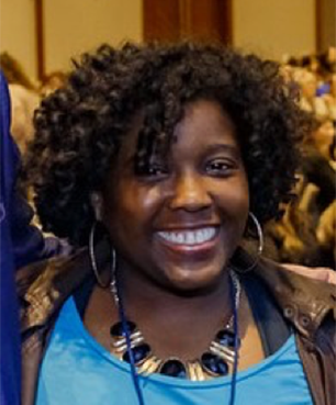 A woman wearing a blue shirt and a necklace smiles for the camera