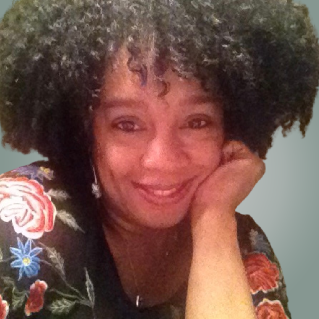 A woman with curly hair is smiling with her hand on her chin.