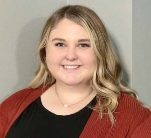A woman wearing a red cardigan and a black shirt is smiling for the camera.