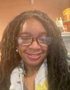 A woman wearing glasses and dreadlocks is smiling for the camera.