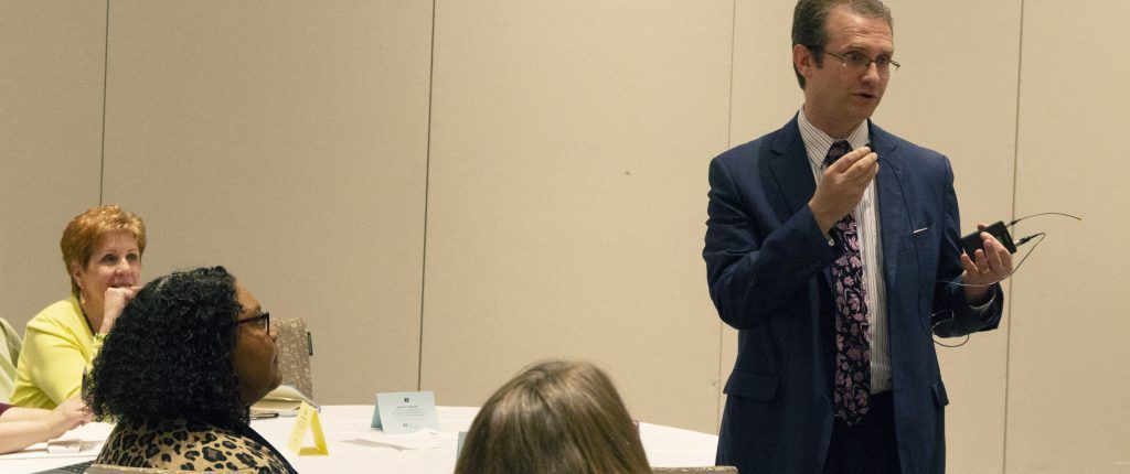 A man in a suit and tie is giving a presentation to a group of people.