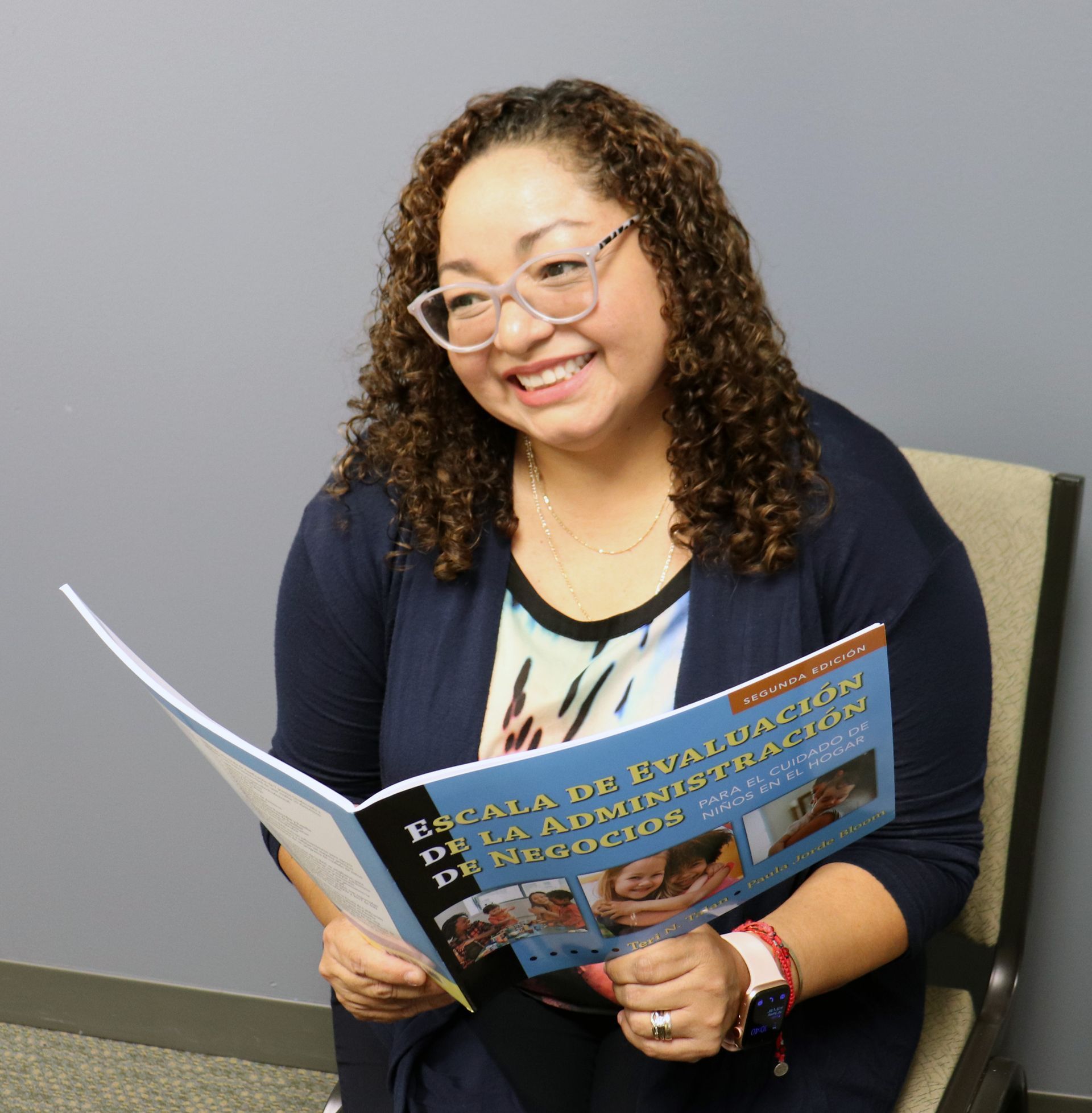 A woman smiling, holding open book.