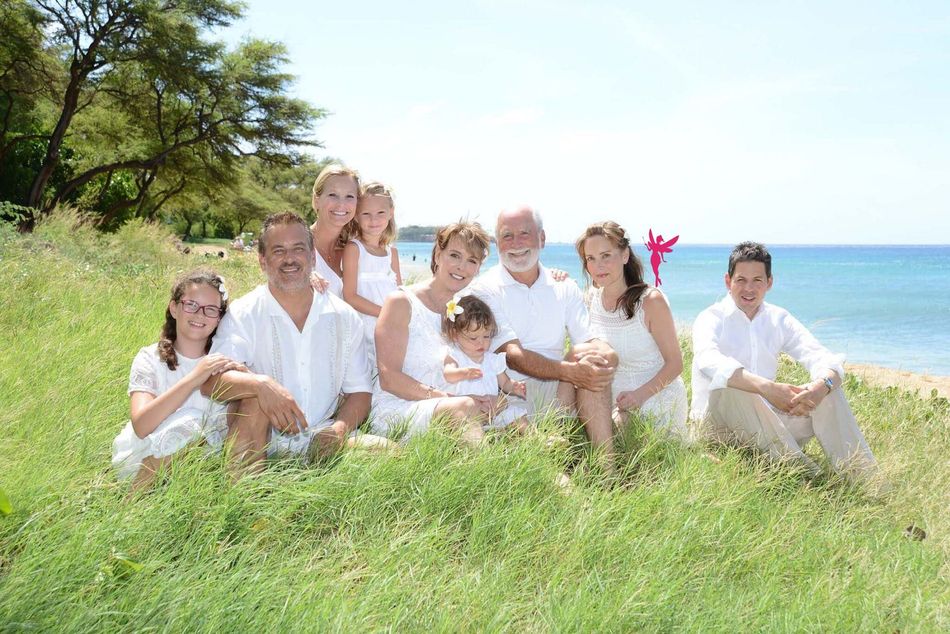 Group of people sitting in tall grass on a sunny hillside, smiling and posing outdoors.