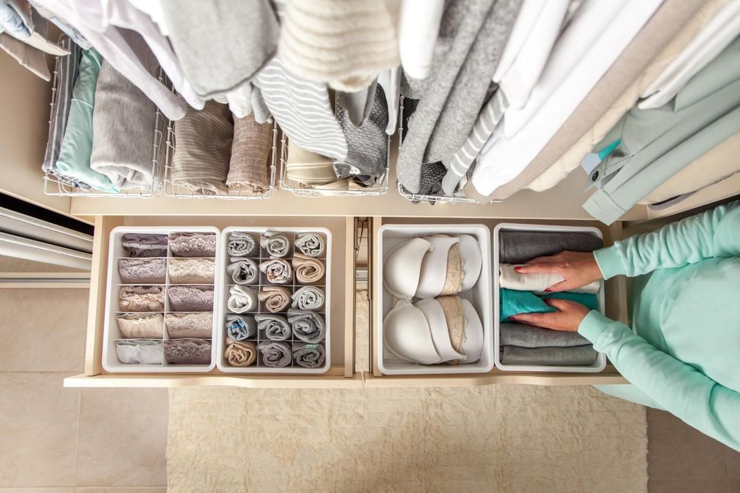 Overhead view of a person organizing folded clothes in a closet drawer system