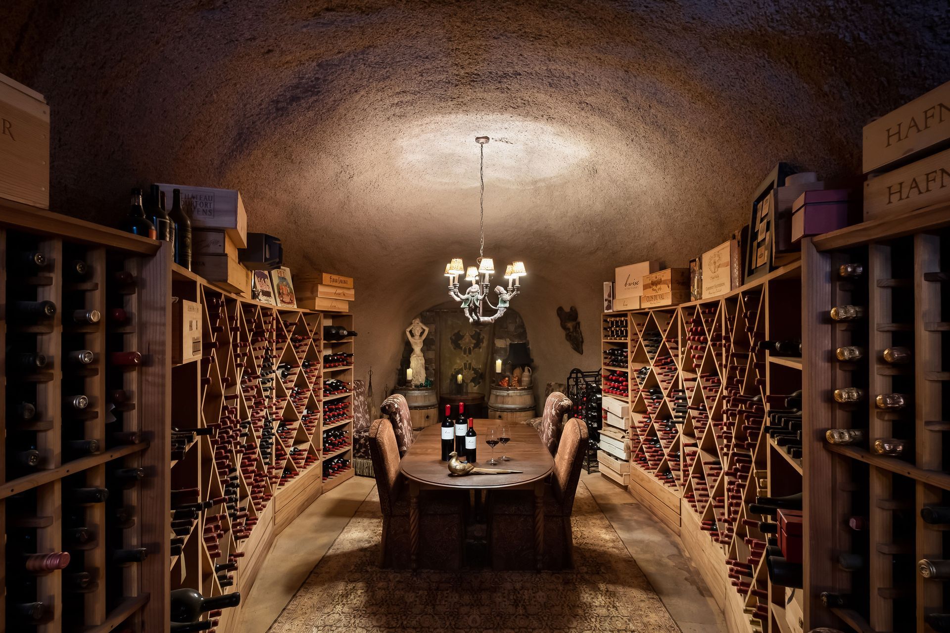 Wine cellar with arched ceiling, wooden racks, and a chandelier over a central tasting table