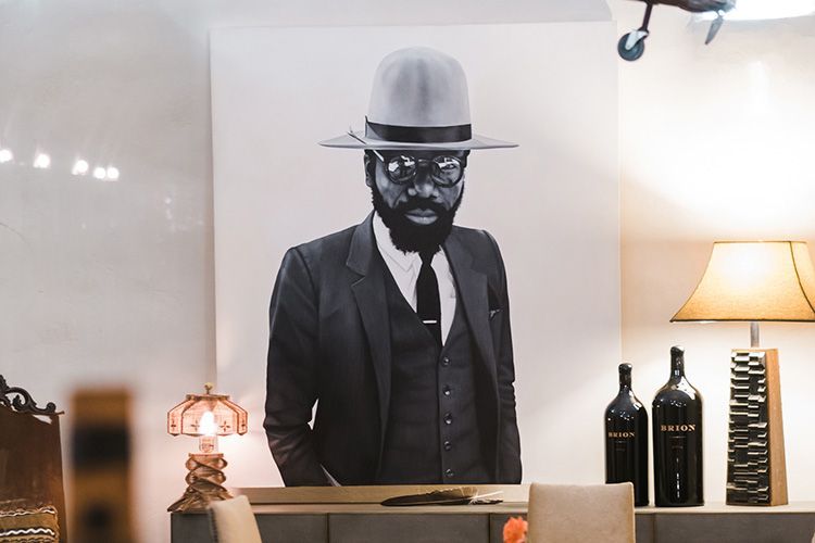 Black-and-white portrait of a suited man in a hat, displayed above a table with lamps and bottles