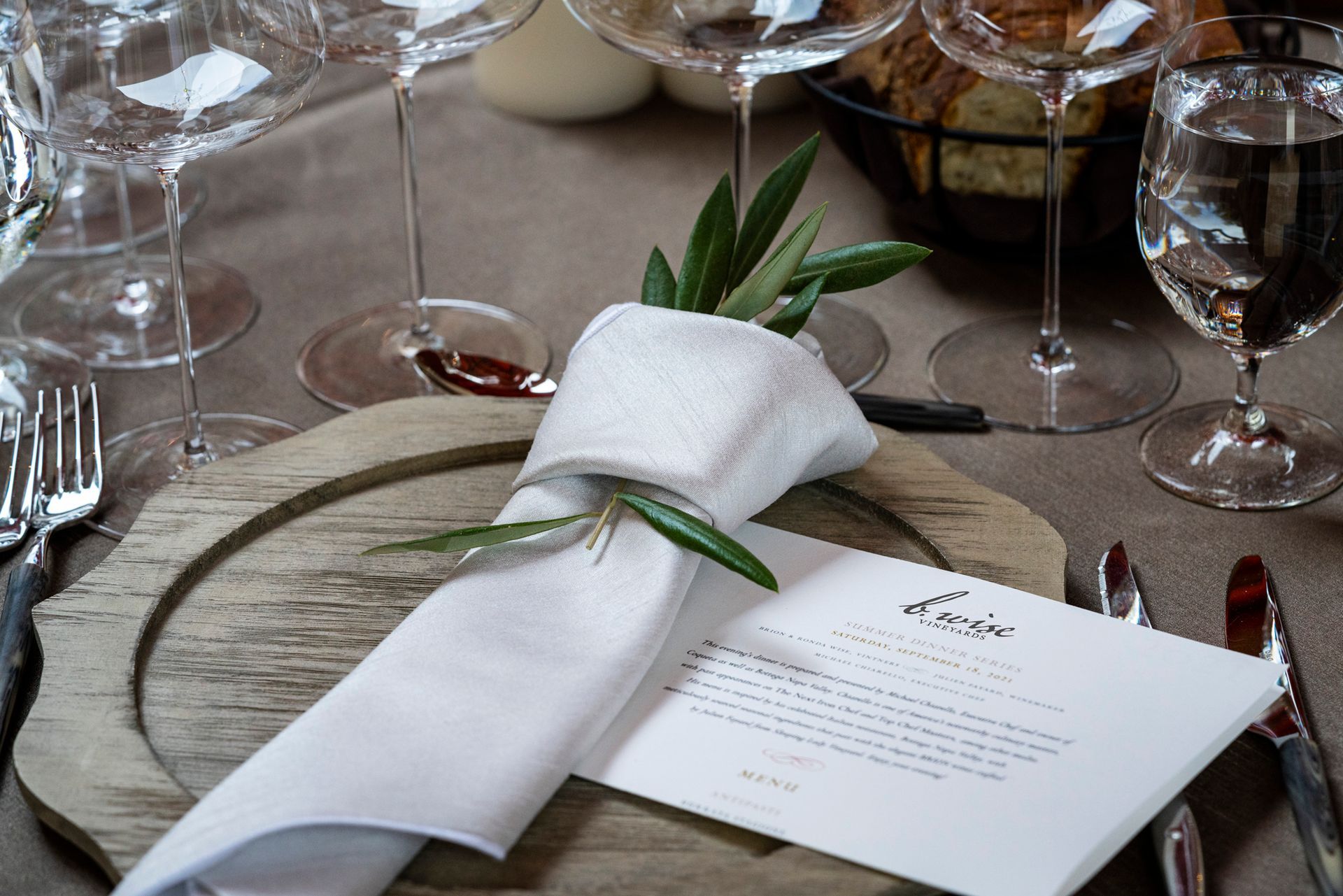 Elegant place setting with rolled white napkin, greenery, glassware, and menu card on a table