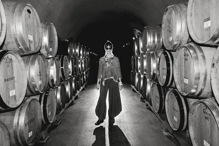 Person walking through a barrel-lined wine cellar, wearing a mask and carrying a bucket.