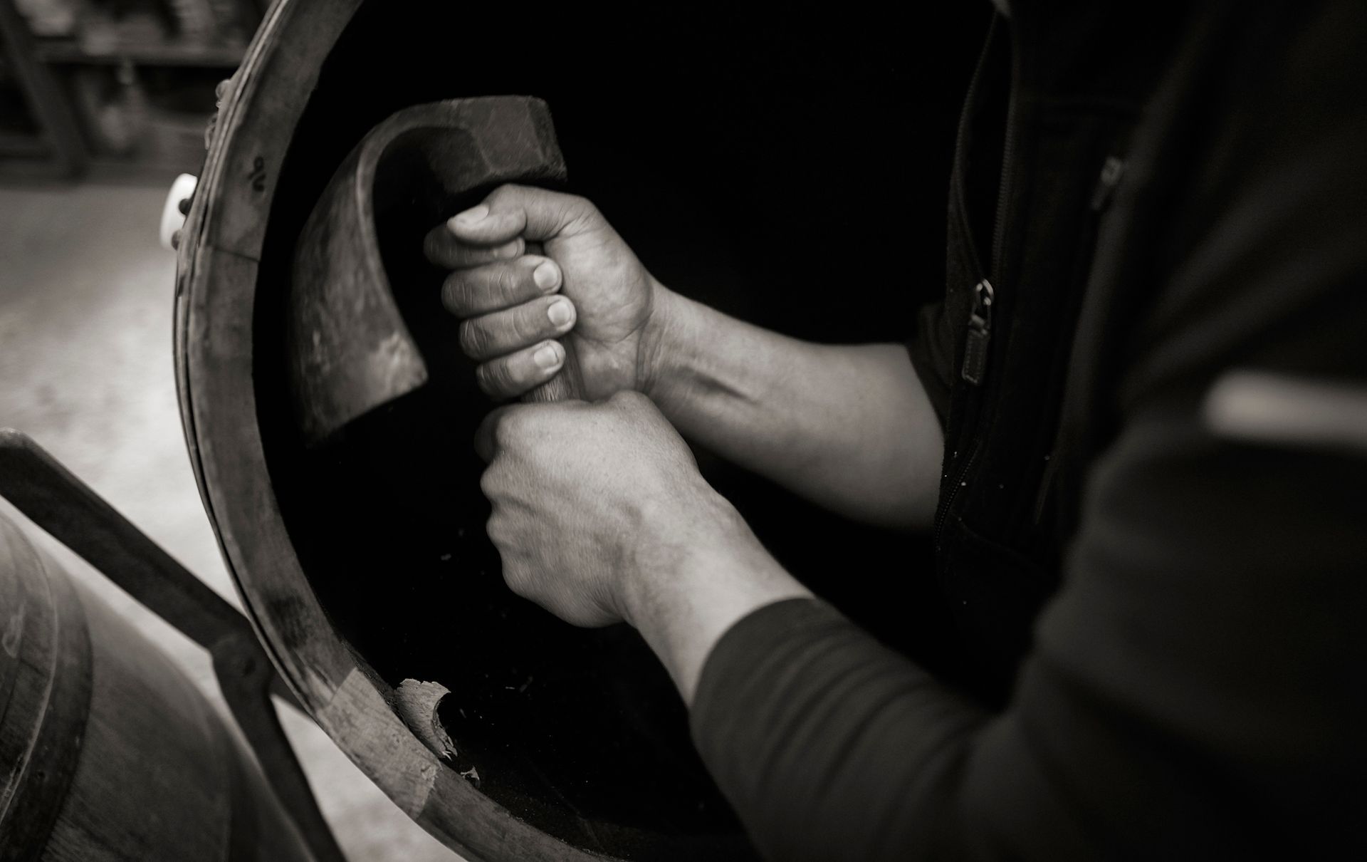Hands gripping the opening of a large dark barrel in a black-and-white industrial scene