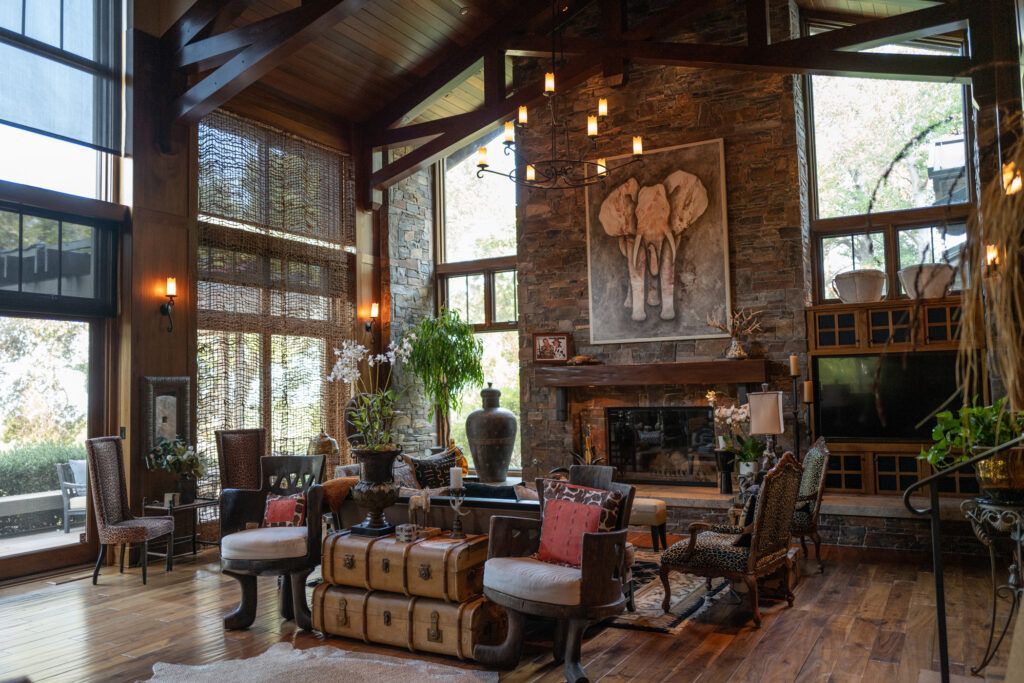 Rustic lodge living room with stone fireplace, tall windows, leather furniture, and warm wood beams