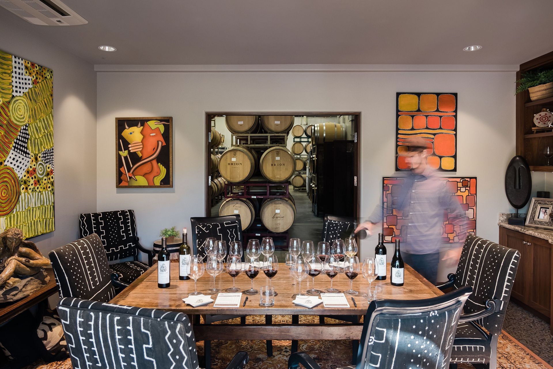 Wine cellar dining room with a long table, black chairs, bottle rack, and colorful wall art