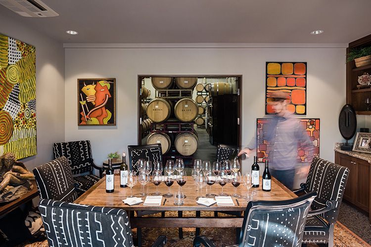 Dining room set for a formal meal, with a long table, patterned chairs, wine glasses, and wall art.