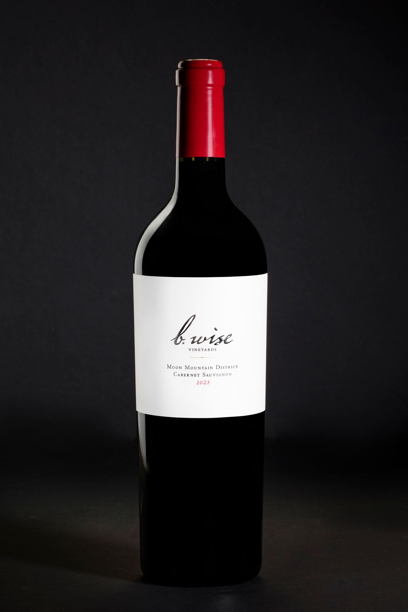 Dark wine bottle with a red neck and white label on a black background