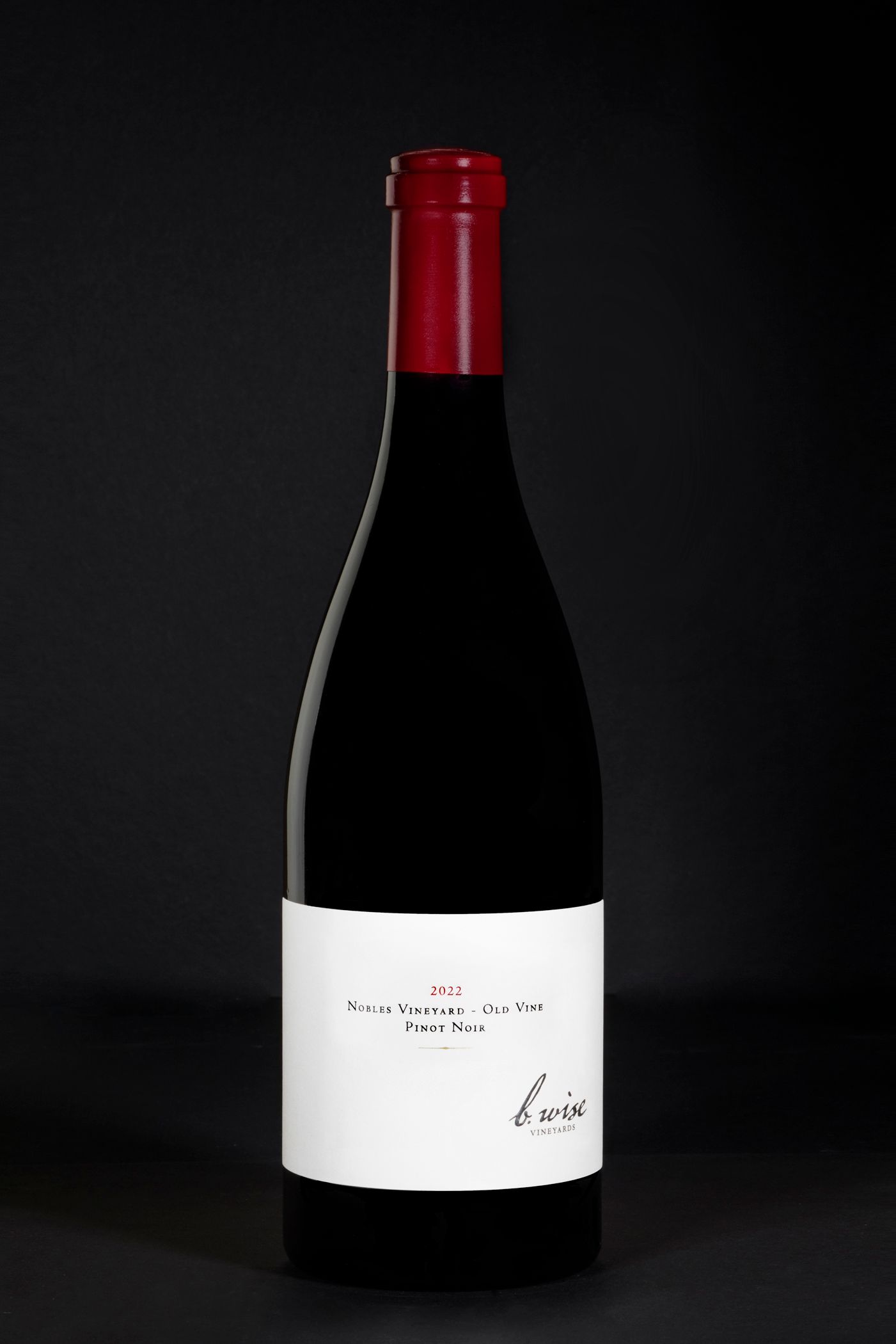 Bottle of red wine with a white label and red foil cap on a dark background