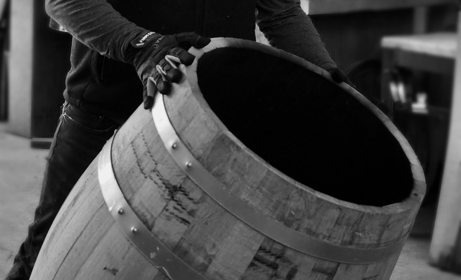 Person tilting a wooden barrel in a workshop, shown in black and white.