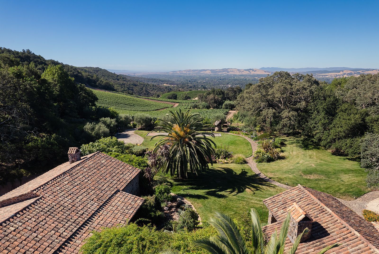 Wide view of lush green gardens with tiled rooftops and distant hills under a clear sky
