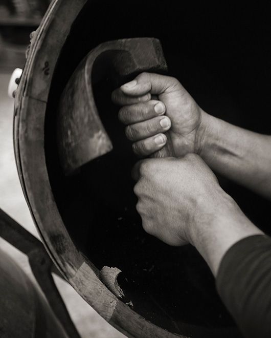 Two hands gripping a large circular metal wheel or tool handle in a dark industrial setting
