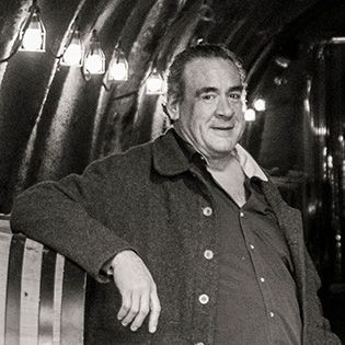 Man leaning on a striped bench in a dim tunnel, lit by overhead lamps, wearing a dark coat.