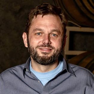 Man with beard in a blue shirt smiling against a warm indoor background