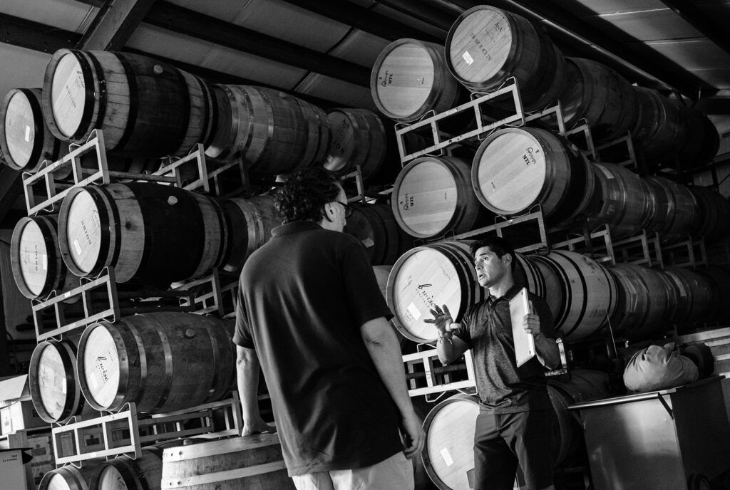 Person standing in a barrel storage room with rows of stacked wooden barrels.