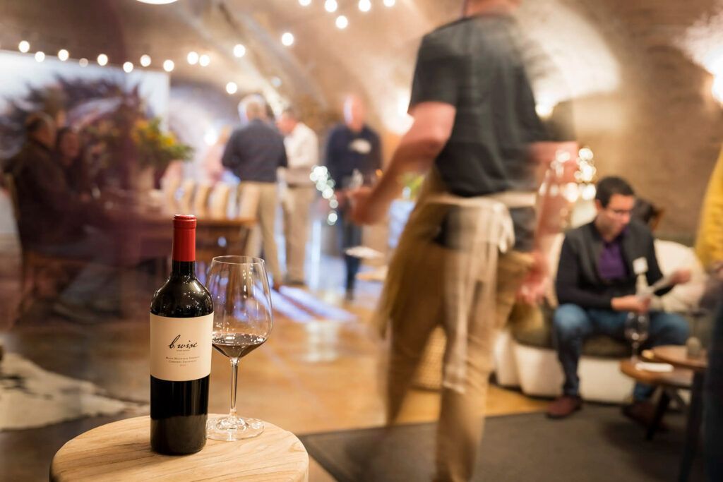 Wine bottle on a wooden table at a softly lit indoor social gathering with blurred people in the background