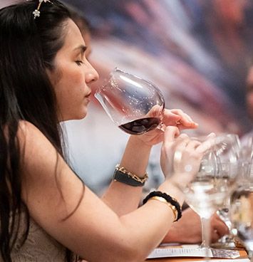 Woman tasting red wine at a table, holding a glass near her lips.