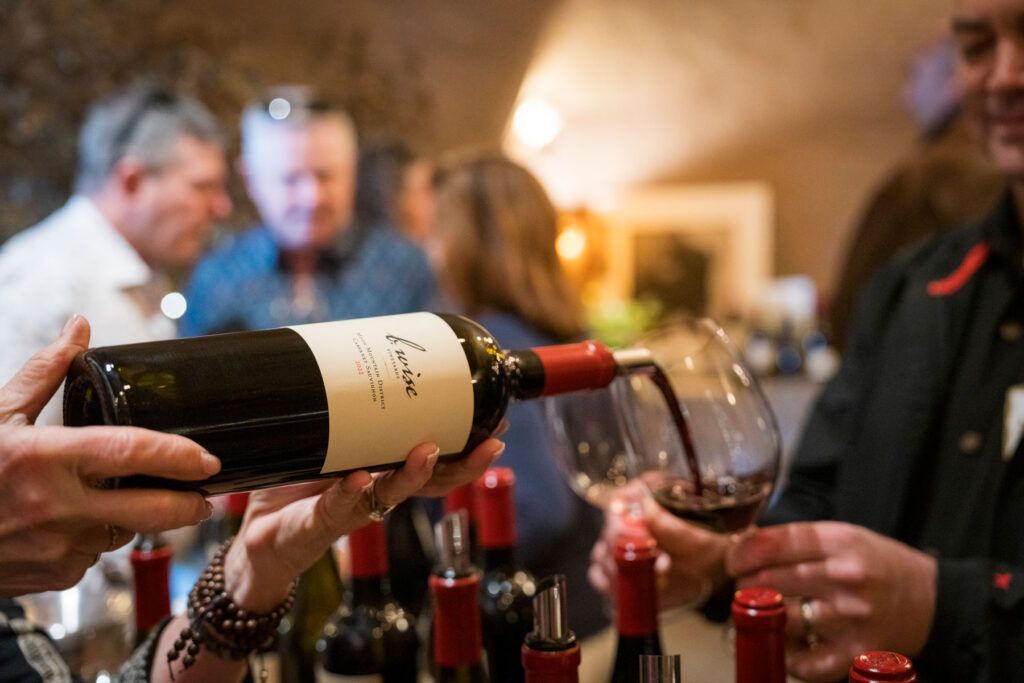Wine being poured into a glass at a social gathering with several people in the background