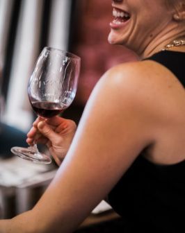 Person in a black top holding a glass of red wine and smiling at a table.