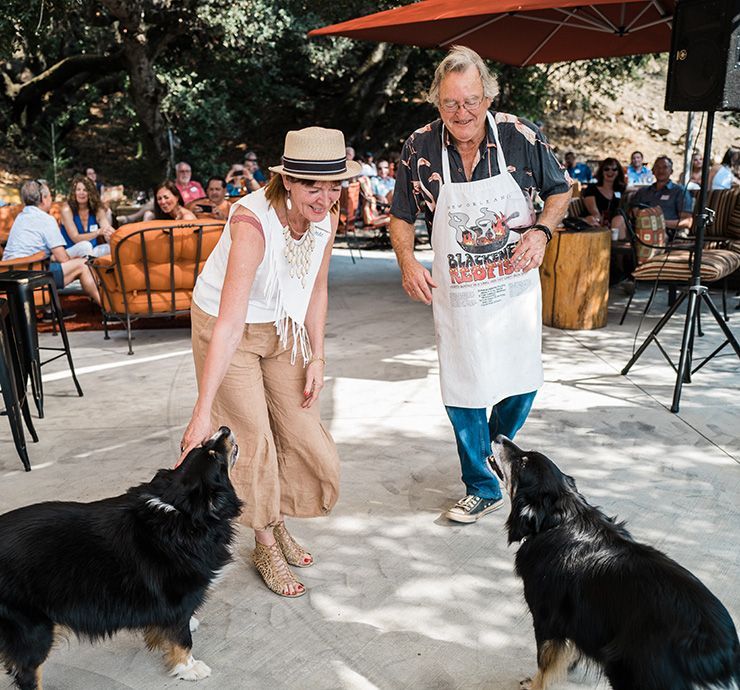 Two women in aprons and hats training two black dogs outdoors at a crowd event