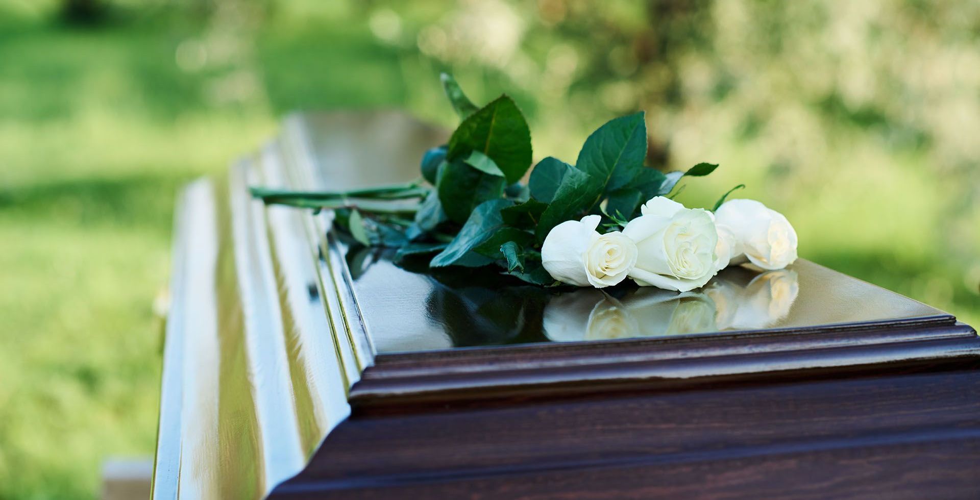 A coffin with white roses and green leaves on it.