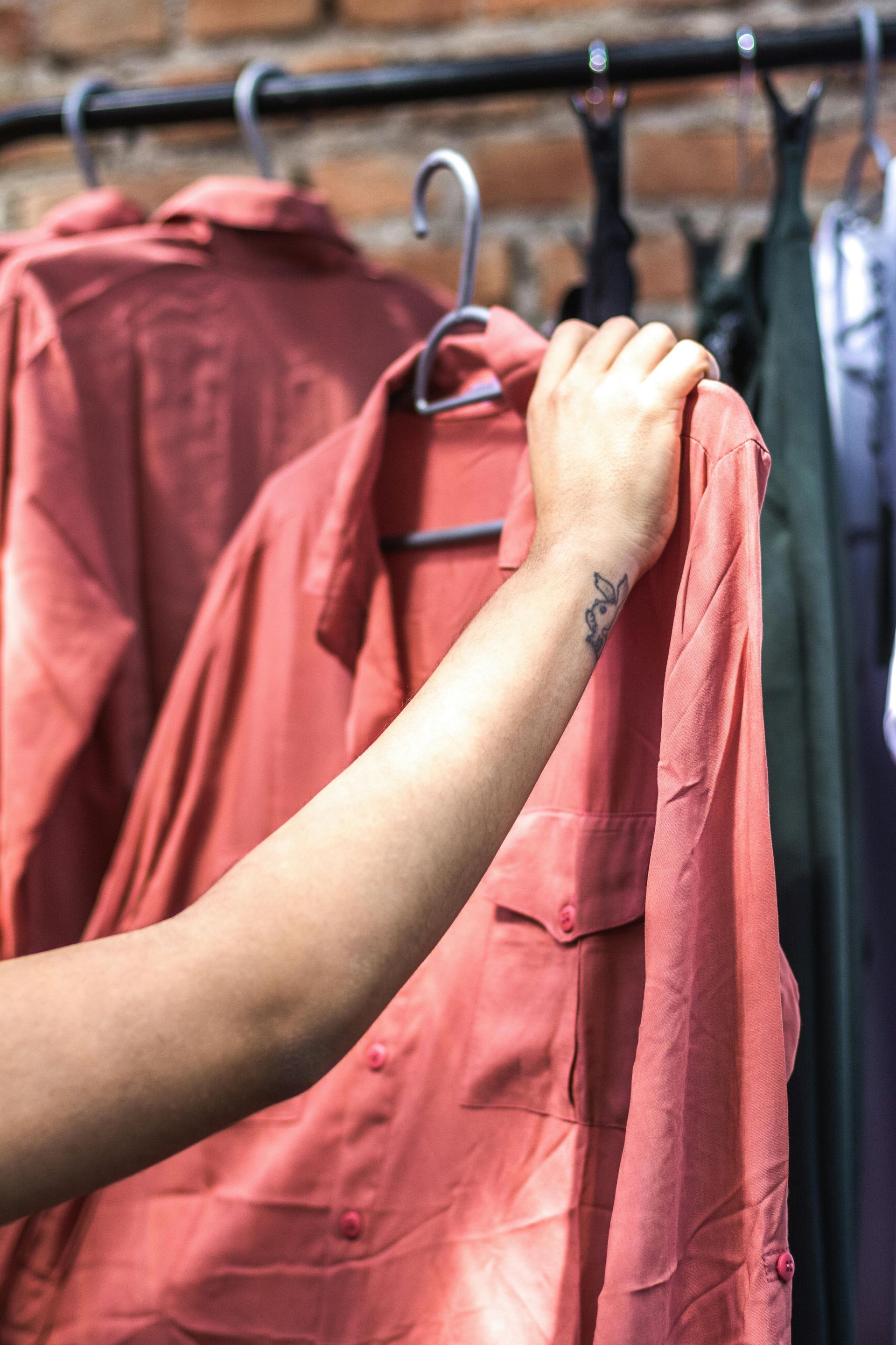 A person with a tattoo on their wrist is holding a red shirt