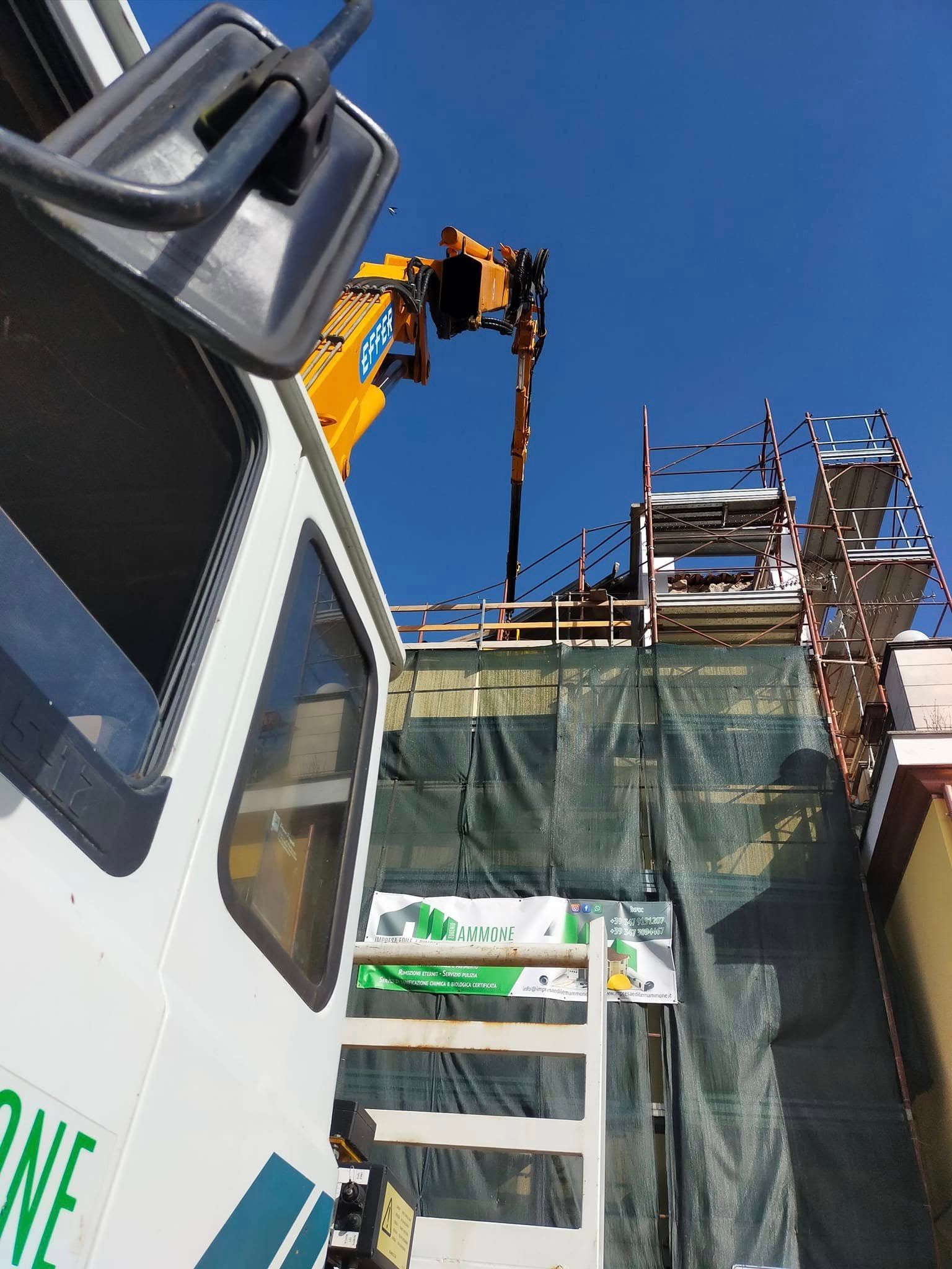 Una gru da costruzione solleva materiali accanto a un camion bianco sotto un cielo azzurro e limpido.