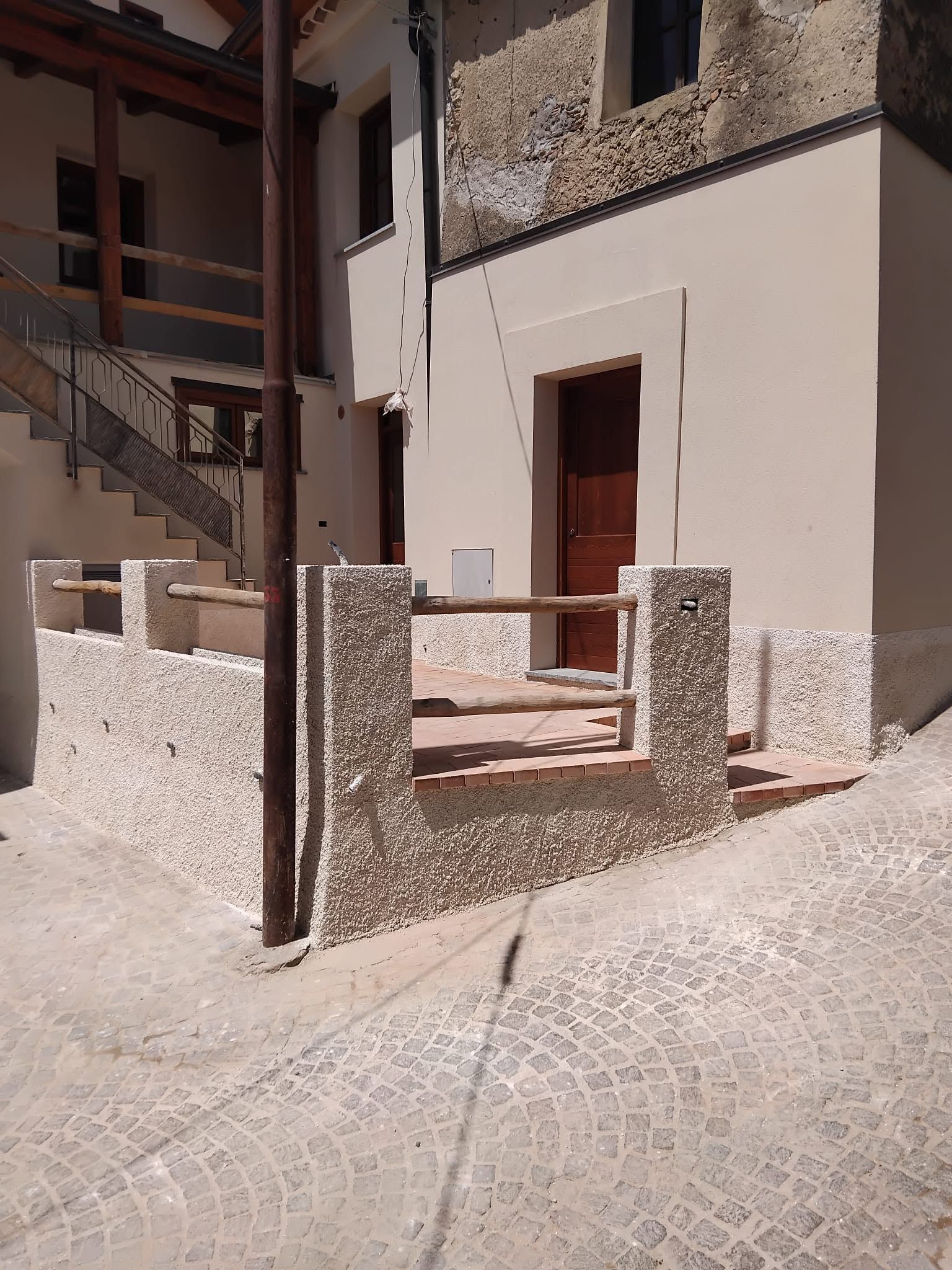 Cortile in pietra con una piccola scalinata, una ringhiera e una porta accanto a un edificio bianco.