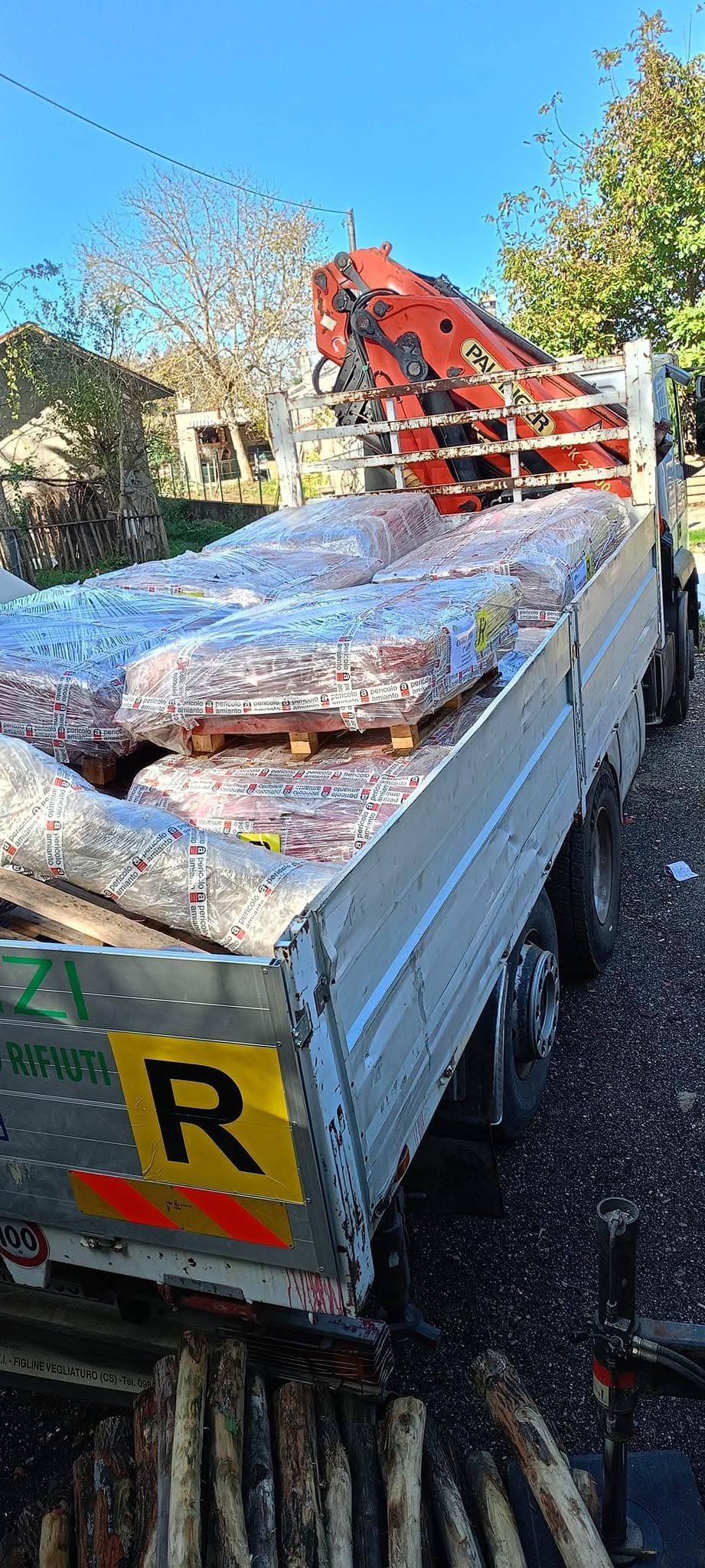 Rimorchio a pianale carico di materiali, con braccio di gru rosso e segnale di pericolo giallo sul retro.