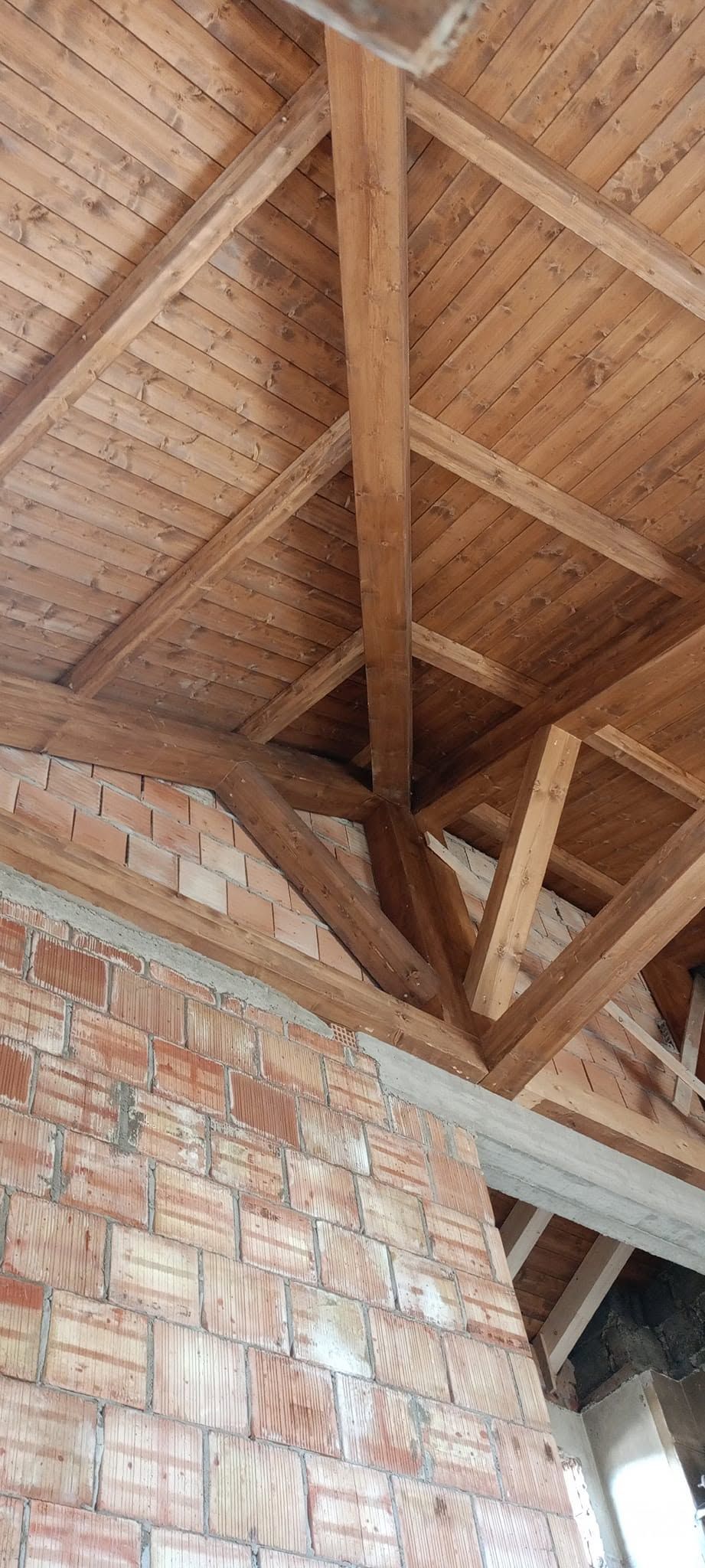 Travi in ​​legno a vista sul soffitto, sopra un muro di mattoni e una porta all'interno di una stanza non rifinita.