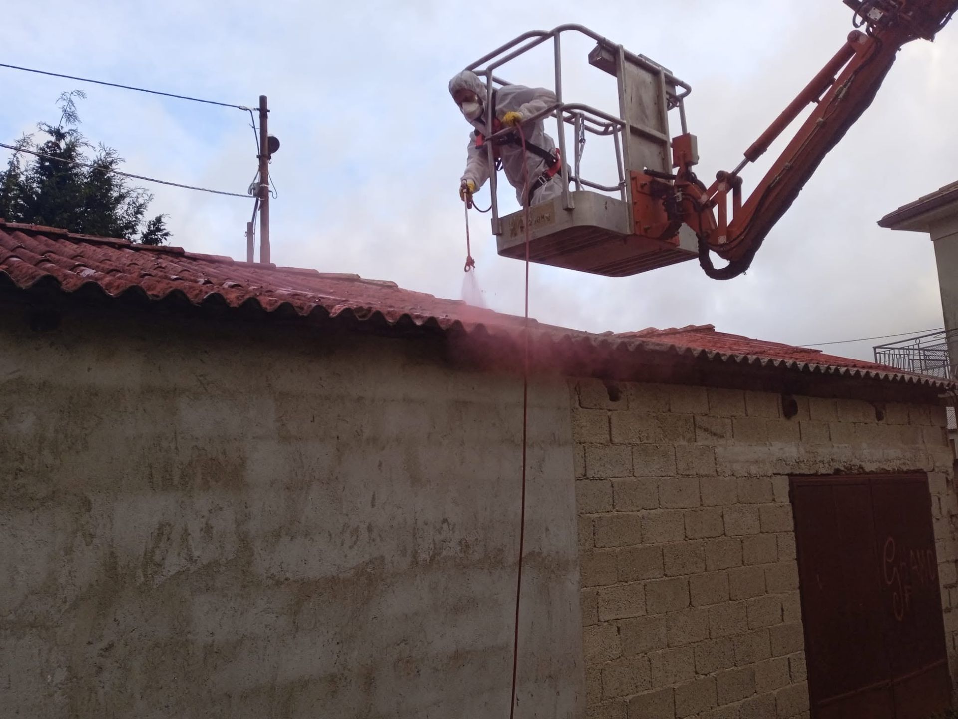 Un operaio, a bordo di una piattaforma aerea, spruzza del liquido nebulizzante sul tetto e sulla parete di una casa.