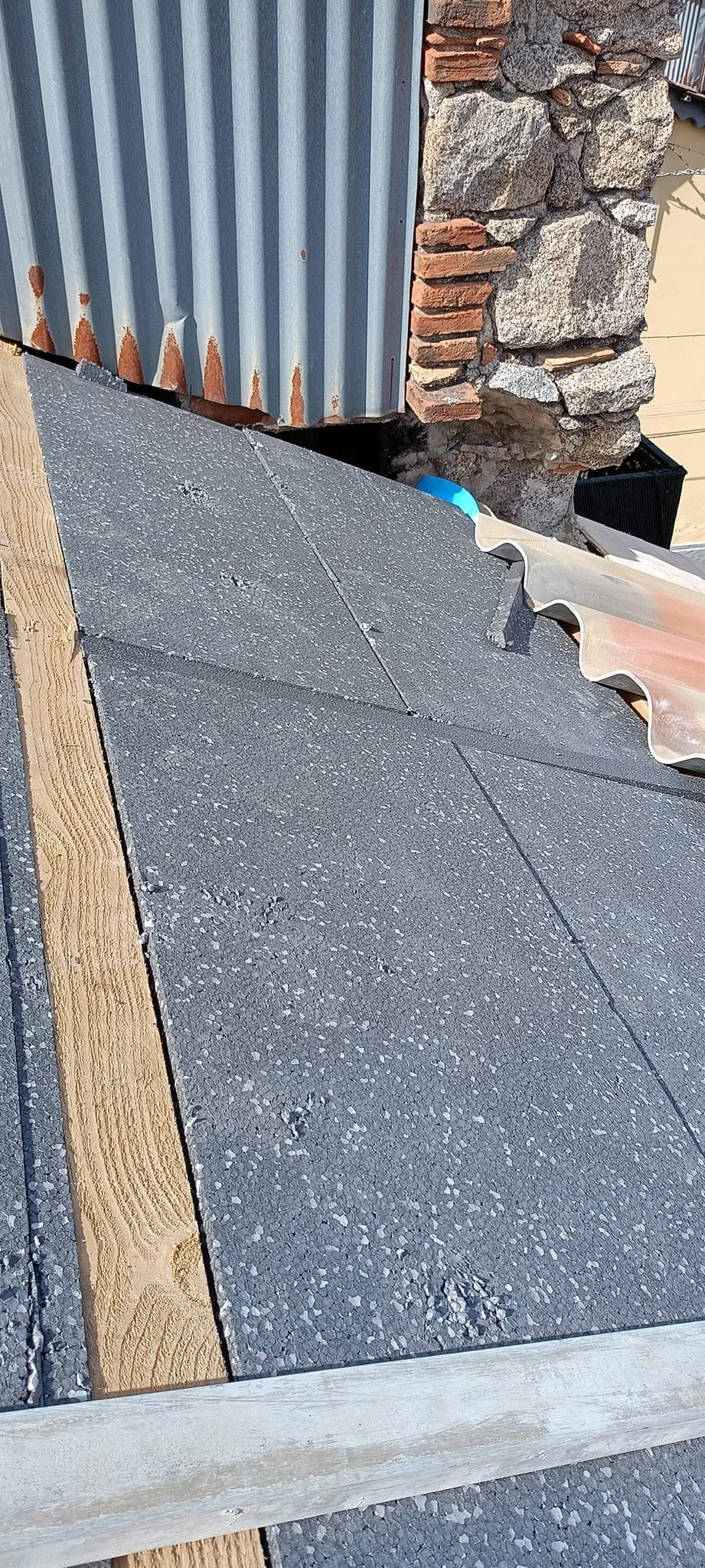 Primo piano di un bordo di asfalto danneggiato accanto a un rivestimento in lamiera ondulata e a un muro di mattoni.