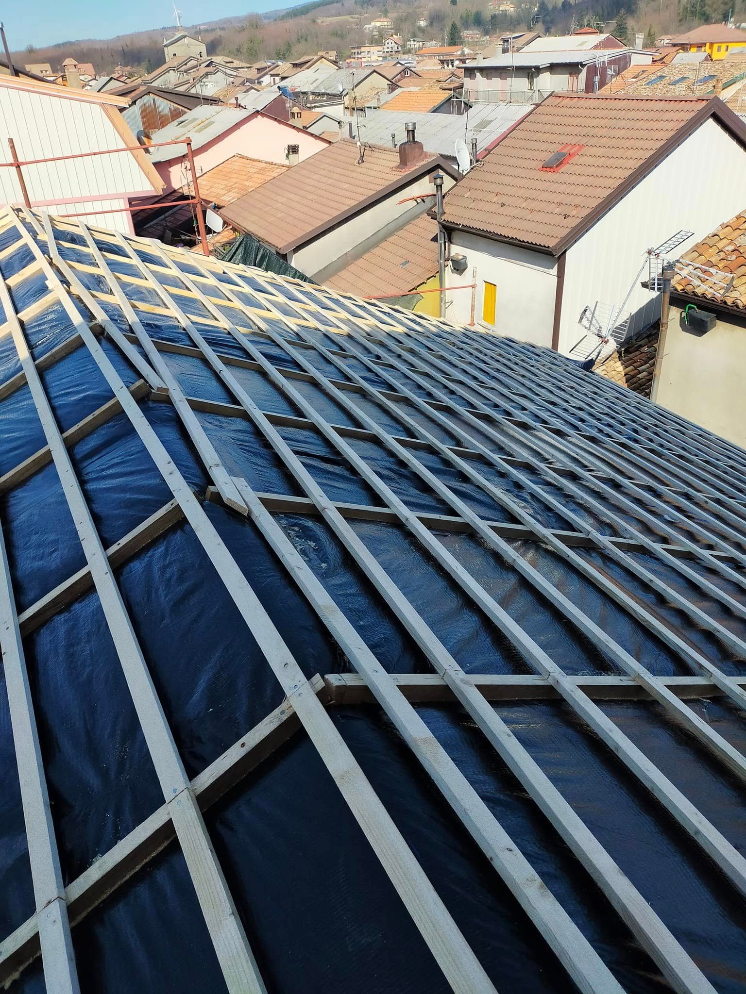 Un tetto di metallo blu si affaccia su una città dai tetti di terracotta sotto un cielo limpido.