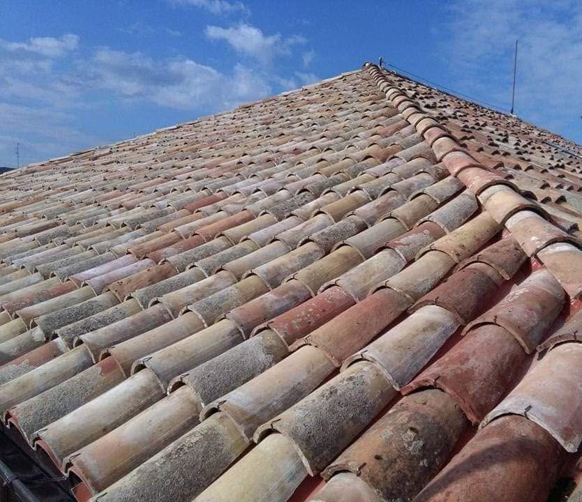 Tegole ondulate in terracotta sotto un cielo azzurro limpido, viste dal colmo del tetto.