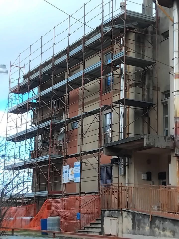 Edificio multipiano in costruzione, con impalcature, rete di sicurezza arancione e struttura metallica.