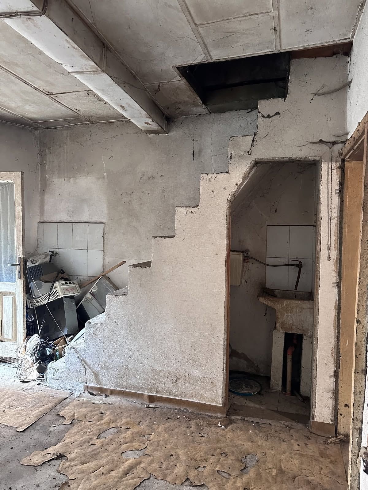 Interno di una stanza danneggiato con pareti sgretolate, soffitto a vista e detriti sul pavimento.