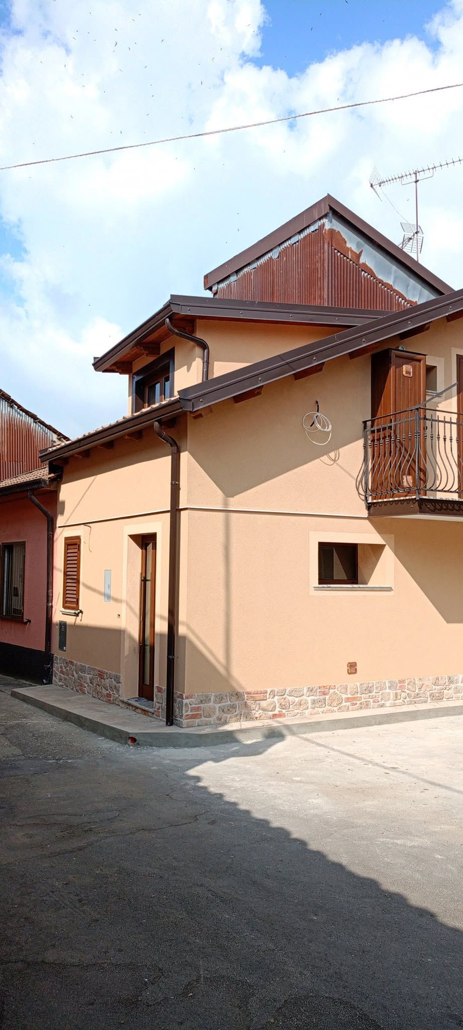 Stretta strada acciottolata accanto a una casa color pesca con stucco e tetto di tegole rosse sotto un cielo azzurro