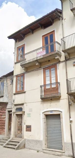 Antica e stretta casa a schiera in stucco con balconi e finestre con persiane, situata in una strada tranquilla.