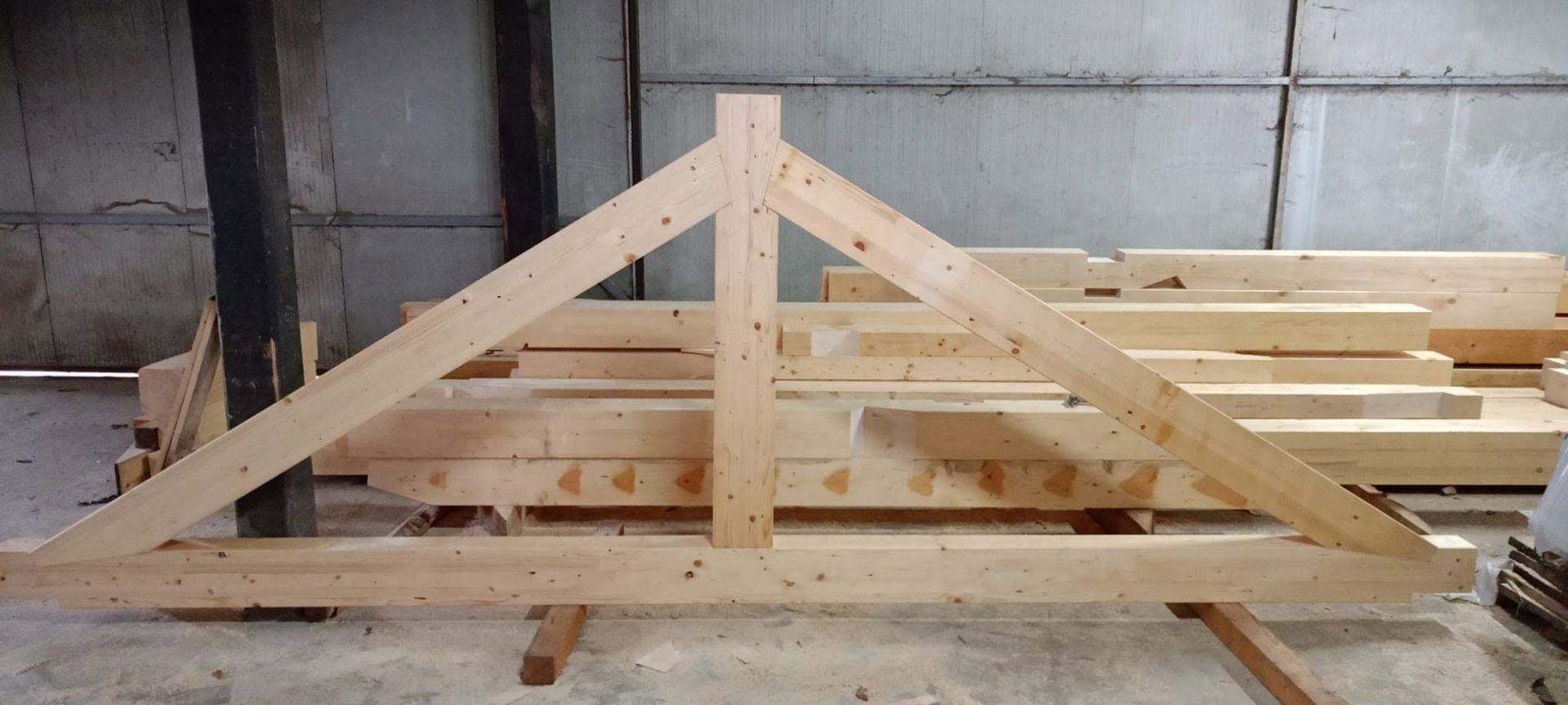 Struttura di capriate in legno appoggiata su una pila di legname in un'officina