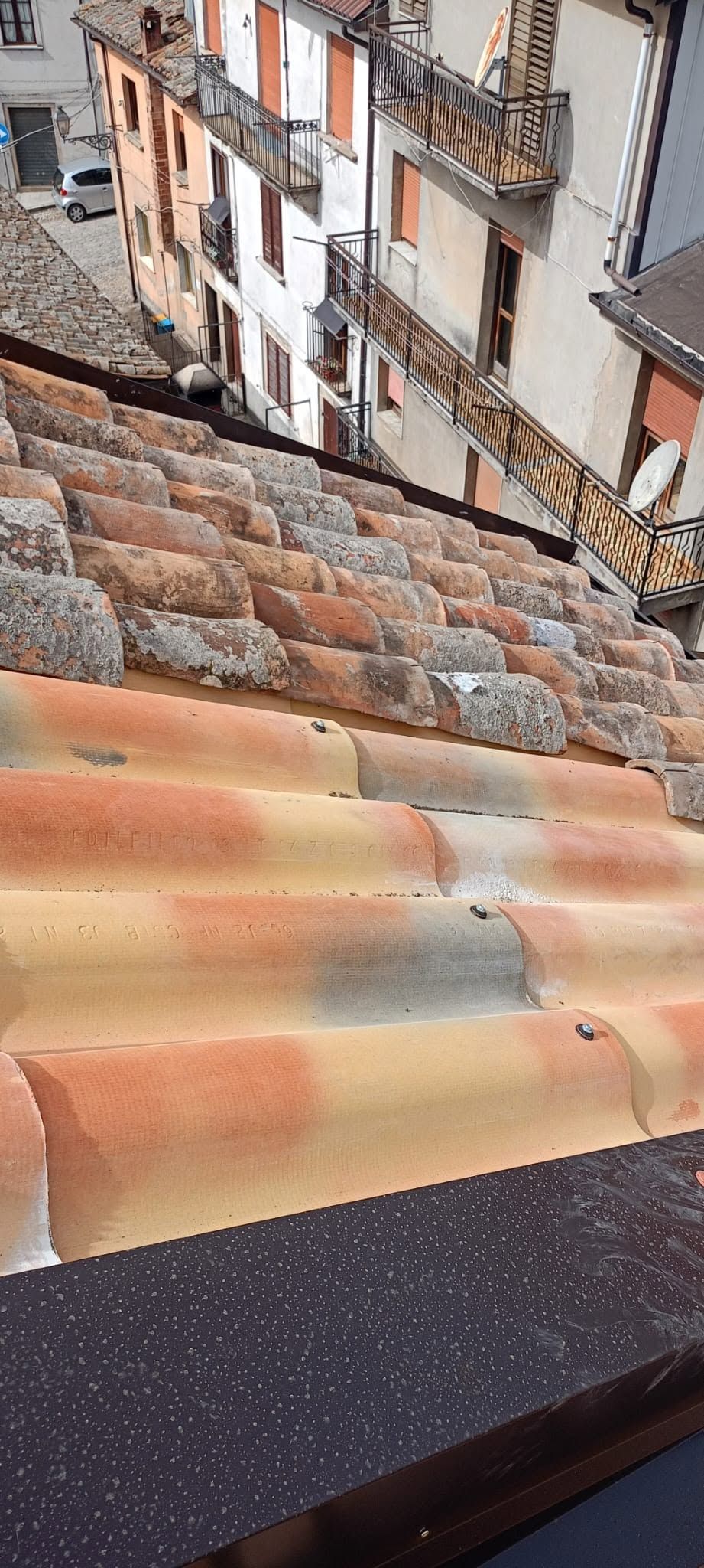 Vista dal tetto, con tegole di argilla arancione, facciate bianche degli edifici e una strada lastricata sottostante.