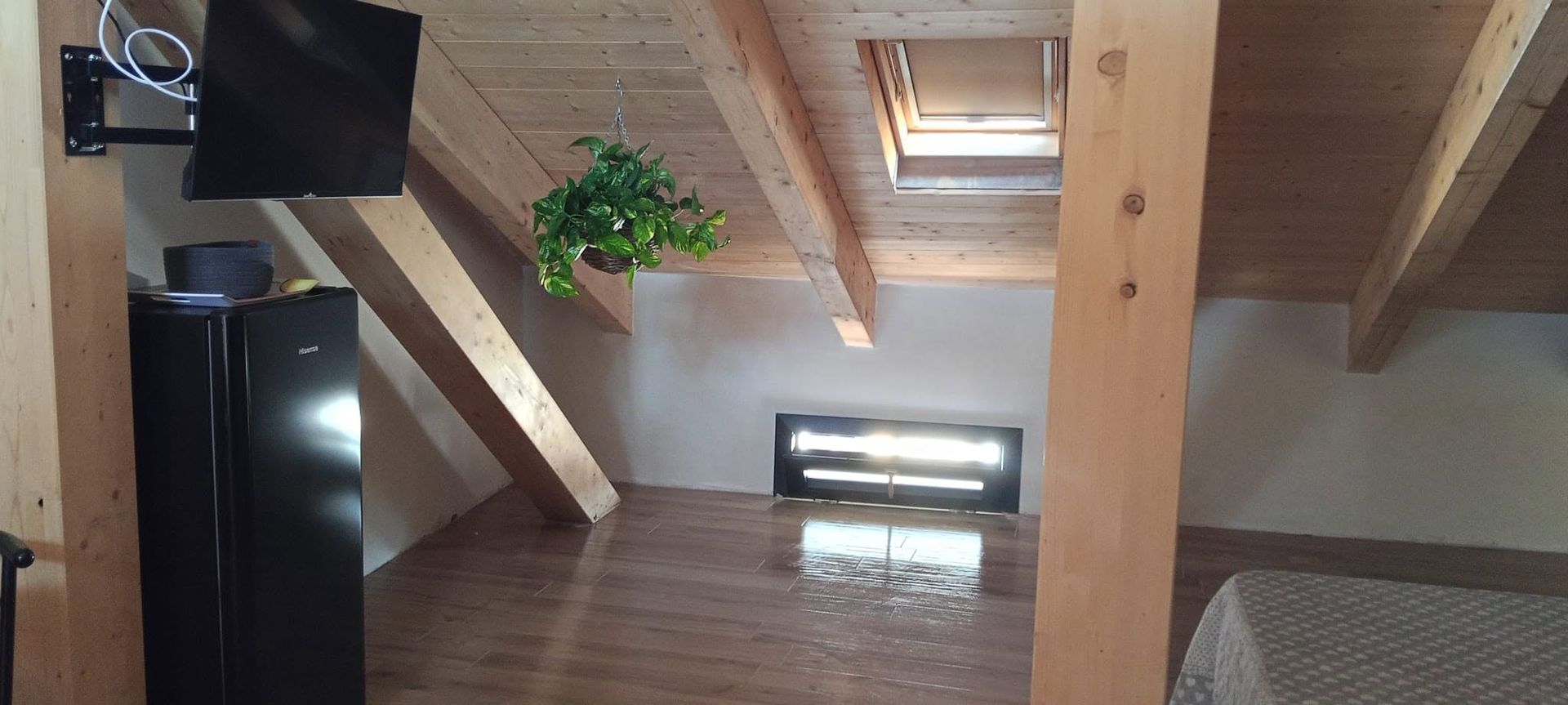 Interno di un loft con travi a vista, lucernario, pianta in vaso e pareti in legno inclinate.