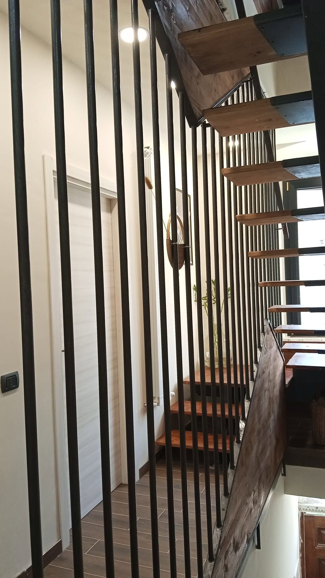 Scala con ringhiera nera e gradini in legno in un luminoso atrio interno.