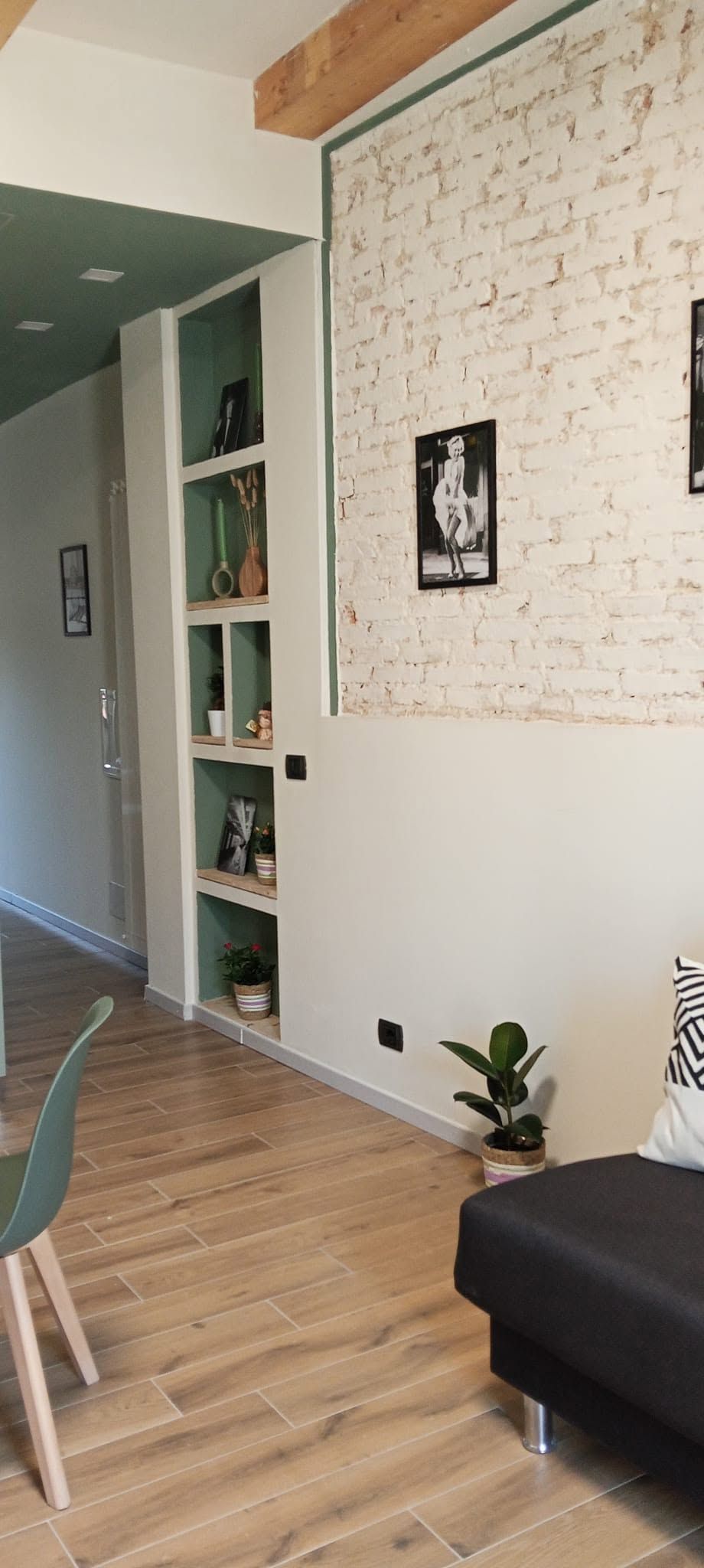 Soggiorno moderno con parete in mattoni bianchi, scaffali a muro, pavimento in legno e divano scuro.